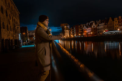 Man standing by illuminated buildings against sky at night
