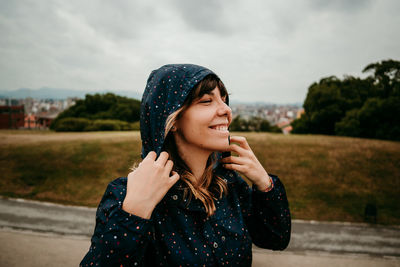 Smiling young woman with raincoat against field