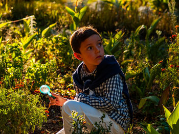 Boy holding magnifying glass while looking away on field