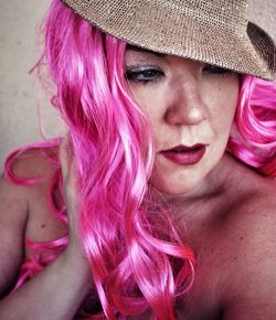 Close-up of shirtless woman wearing wig looking away against wall