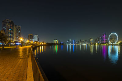 Illuminated city by river against sky at night