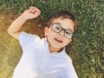 Directly above portrait of boy in eyeglasses lying on grassy field at public park