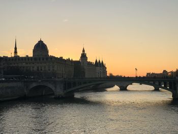 Bridge over river in city against sky during sunset