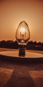 Close-up of illuminated light bulb against sky during sunset