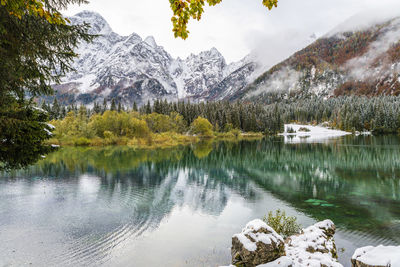 Between autumn and winter. warm and cold reflections of snow on lake fusine.