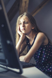 Thoughtful girl using computer while sitting on table