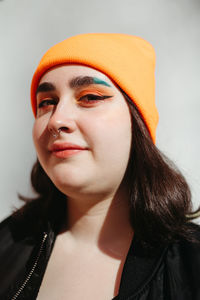 Young smiling female with green dyed hair wearing a beanie and a black jacket looking at camera while standing near grey wall on sunny street