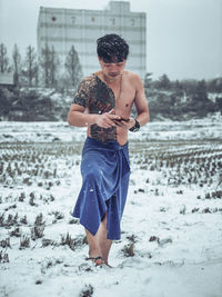 Full length of shirtless man standing on snow covered land