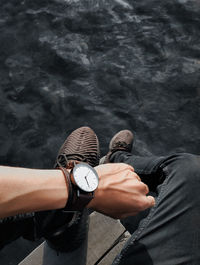 Low section of man wearing wristwatch sitting by lake