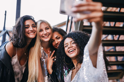Low angle view of cheerful young female friends taking selfie with mobile phone on staircase