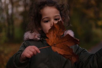 Contemplating girl looking at maple leaf in park during autumn