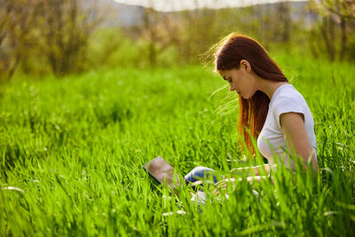 Side view of young woman with arms outstretched on grassy field