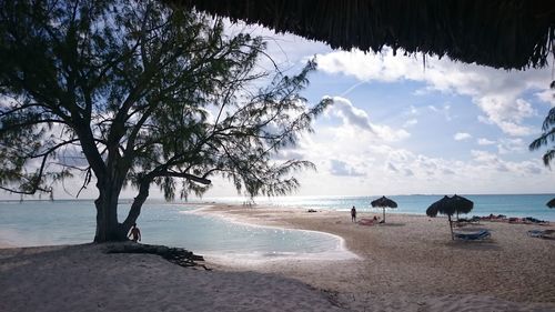 Scenic view of beach against cloudy sky seen through thatched roof parasol