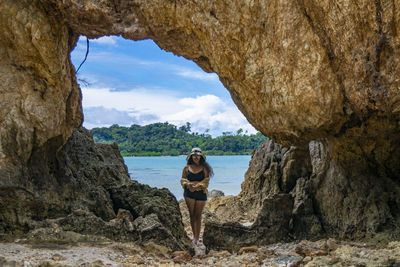 Full length of woman wearing bikini standing by rock formations at beach