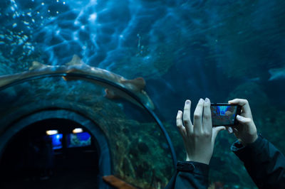 Cropped hands photographing in tunnel aquarium