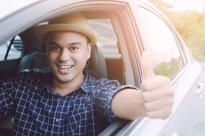 Portrait of smiling man showing thumbs up while sitting in car