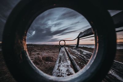 Empty bench on field against cloudy sky during sunset