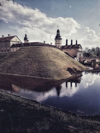 Buildings by river against cloudy sky