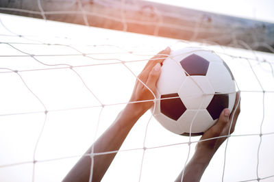 Cropped hands holding soccer ball touching goal post