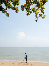 Scenic view of a man with a metal detector on the beach against clear sky