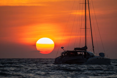 Silhouette sailboat in sea against orange sky