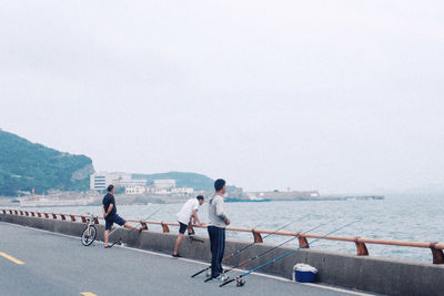 People on road by sea against clear sky