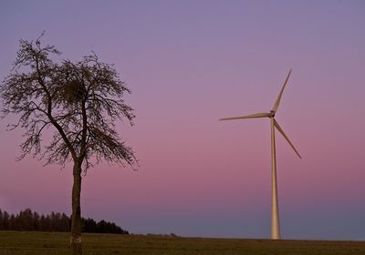 Wind turbines on field against sky at sunset