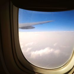 View of airplane wing against cloudy sky seen through window