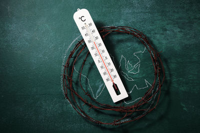 High angle view of rusty barbed wire with globe drawing and thermometer on blackboard