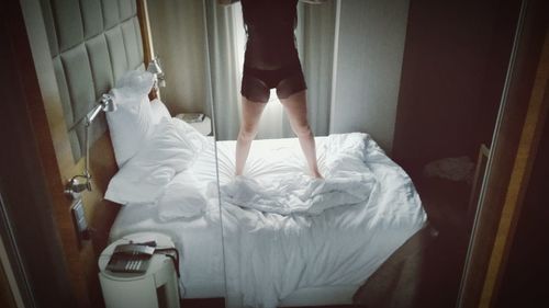 Low section of man standing on bed