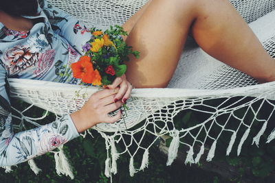 Midsection of woman holding flowers while resting on hammock