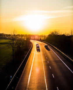 Vehicles on road against sky during sunset