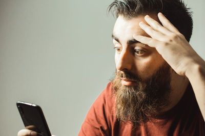 Surprised young man looking at mobile phone against standing against gray background