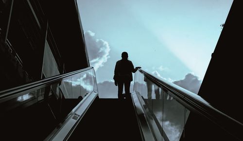 Low angle view of silhouette woman standing on escalator against sky