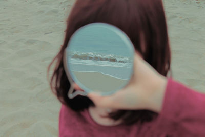 Close-up girl holding mirror with reflection of sea at beach