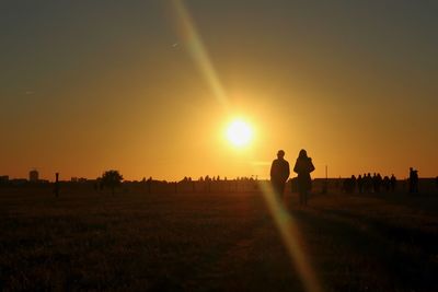 Silhouette people on field against sky during sunset