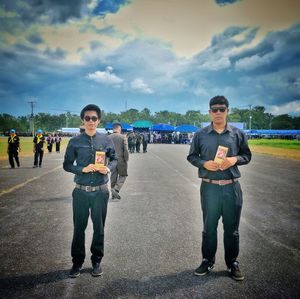 Full length portrait of friends standing on road against sky