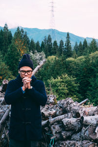 Man praying while standing against logs in forest