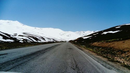 Road amidst snowcapped mountains against clear blue sky