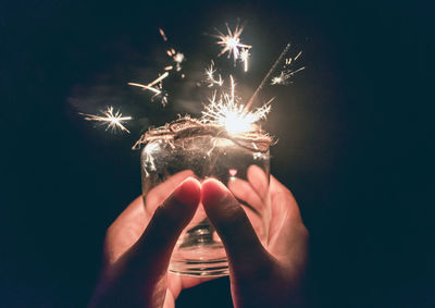 Cropped hands of person holding illuminated sparkler in jar at night