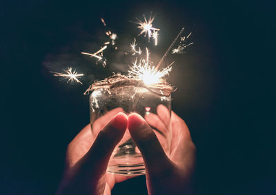 Person hand holding firework display at night