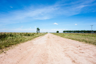 Dirt road amidst field against sky