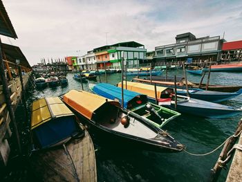 Boats moored at harbor by buildings against sky