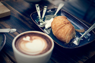 Croissant on wooden table with a cup of coffee, vintage color tone.