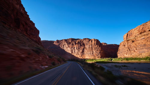 Road leading towards mountains against clear sky