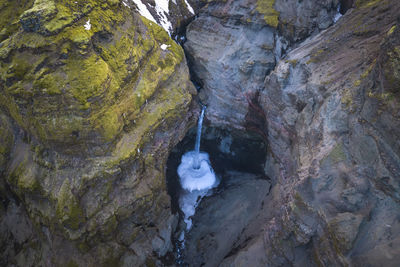 From above stream of clean water falling from rough stony cliffs covered with moss in countryside of iceland