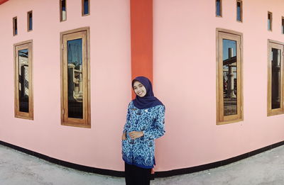 Portrait of smiling woman standing against building in city