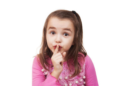 Portrait of cute girl with finger on lips gesturing silence against white background