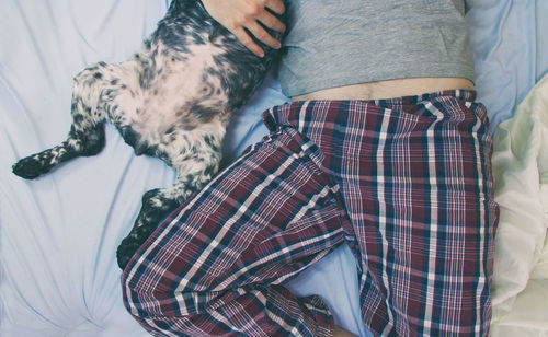 Low section of woman with dog relaxing on bed at home