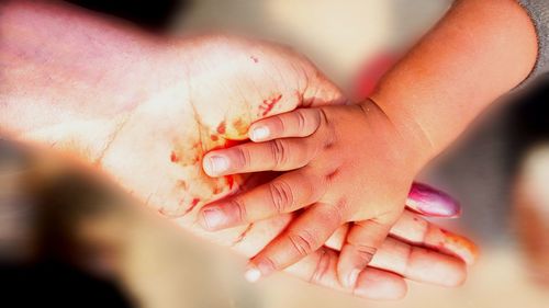 Cropped hand of mother and baby girl with blood at home